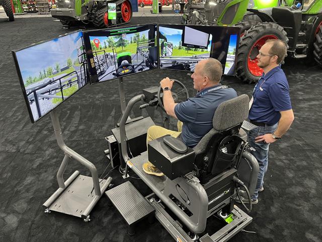 DTN/Progressive Farmer Senior Editor Dan Miller (left) leaves the yard in Fendt's Rogator 900 series sprayer simulator. He missed the tanks and vehicles coming down the highway, but soon crushed a stop sign, twice. (Photo courtesy of Fendt)